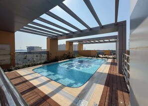 Ein Pool auf dem Dach mit einer Pergola, einer Holzterrasse und Blick auf die Stadtlandschaft.