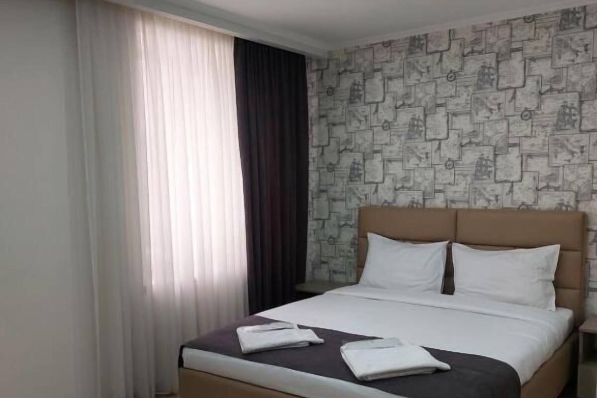 Una cama bien hecha con cabecera, una ventana con cortinas y una pared con diseño.
