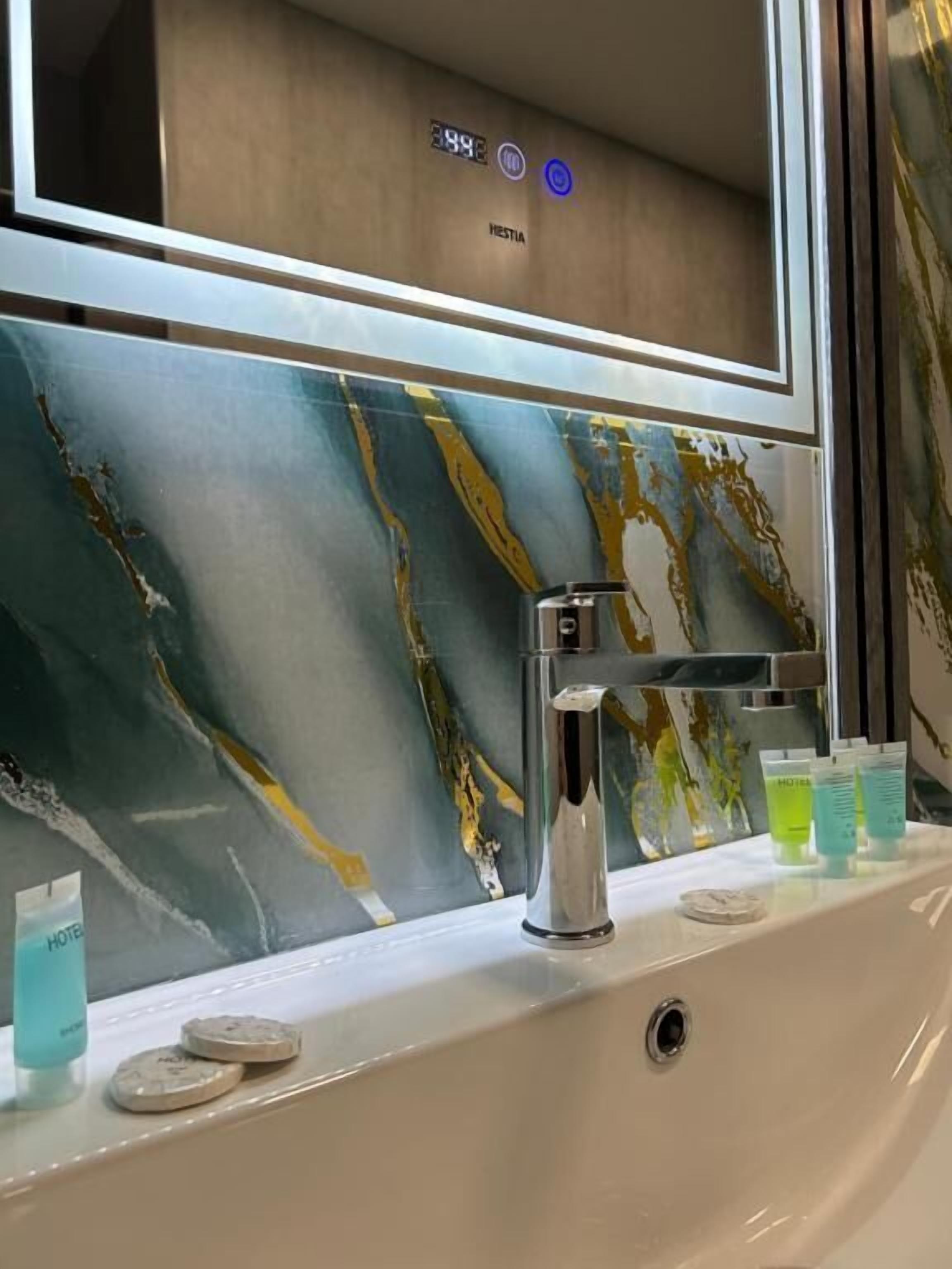 Une salle de bain avec un pare-baignoire en marbre, un robinet moderne et des articles de toilette posés sur le comptoir.