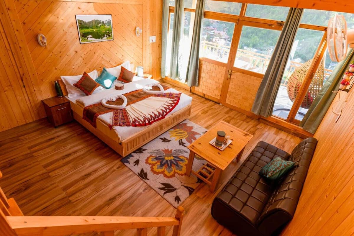 A wooden cabin room with a bed, a sofa, a small table, and a window with a view.