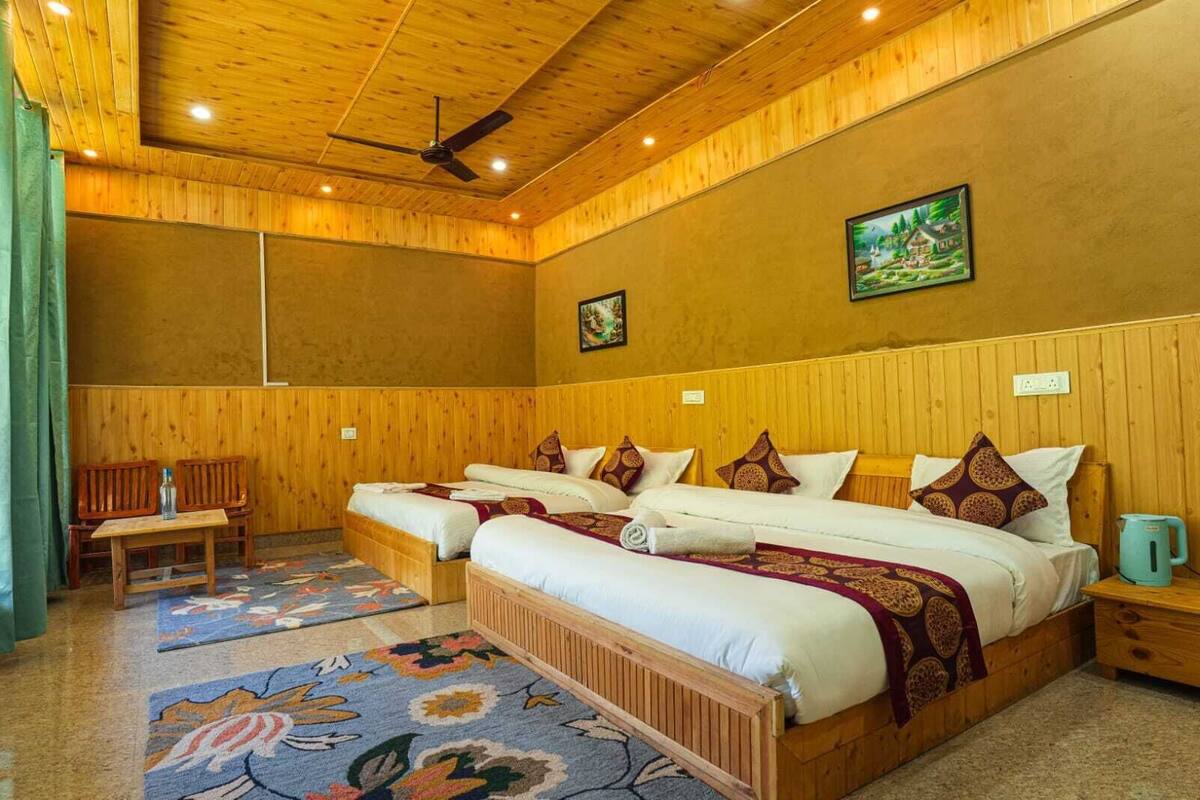 A room with wooden paneling, two beds with patterned bedding, a ceiling fan, and a painting on the wall.