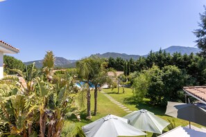 Ein Garten mit Pool, Sonnenschirmen und Bergen im Hintergrund.