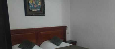 Una habitación con dos camas, un cabecero de madera, un cuadro en la pared y suelo de baldosas.