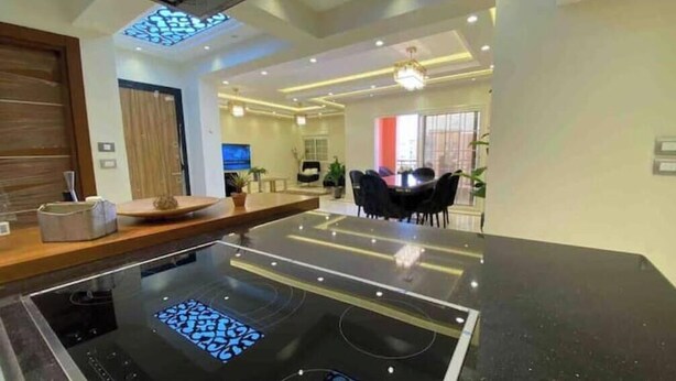 A modern kitchen with a central island, a dining area with a table and chairs, and a large window. - Luxury Dreamland Retreat – Spacious Pool Stay Near the Pyramids (Giza Governorate)