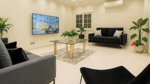 A modern living room with a glass coffee table, black sofas, and a large flat-screen TV mounted on the wall. - Luxury Dreamland Retreat – Spacious Pool Stay Near the Pyramids (Giza Governorate)