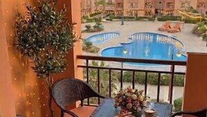 A balcony with a pool, chairs, a table with food, and a view of apartment buildings. - Luxury Dreamland Retreat – Spacious Pool Stay Near the Pyramids (Giza Governorate)