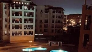 A rooftop swimming pool with a view of surrounding buildings at night. - Luxury Dreamland Retreat – Spacious Pool Stay Near the Pyramids (Giza Governorate)