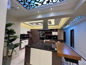 A modern kitchen with a central island, dark cabinetry, and a skylight. - Luxury Dreamland Retreat – Spacious Pool Stay Near the Pyramids (Giza Governorate)