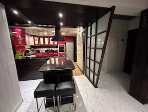 A modern kitchen with a central island, bar stools, and a view of the adjacent living area. - Pool View Villa Apartment – Private Garden Escape in Dreamland (Giza Governorate)