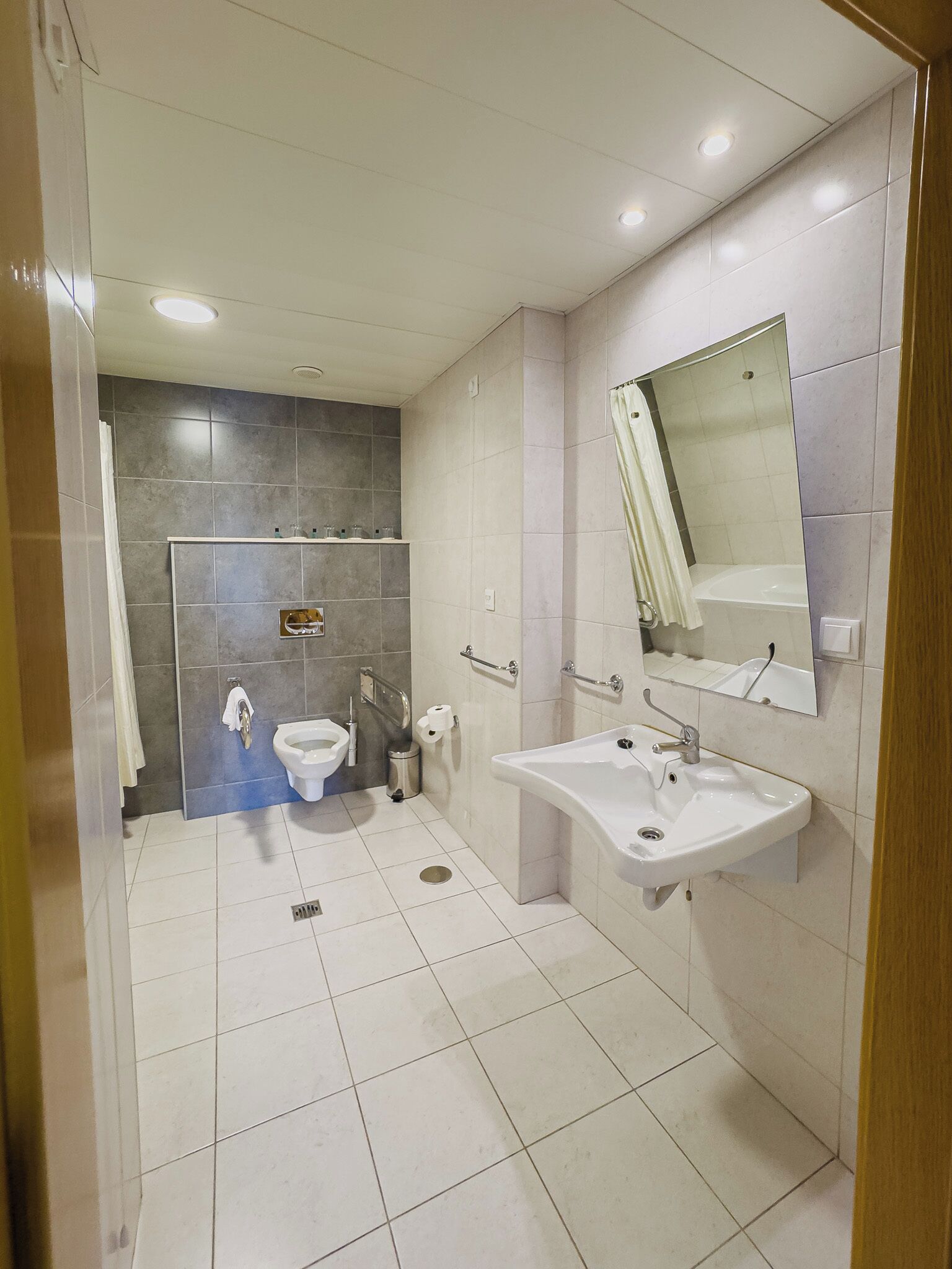 Une salle de bain moderne équipée de toilettes, d’un bidet, d’un lavabo, d’un miroir et de murs carrelés.