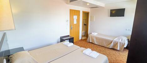 Habitación de hotel con dos camas, un escritorio, una silla, un televisor y zona de ducha.