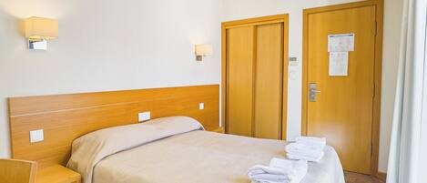 A hotel room with a bed, a desk, two doors, and a patterned carpet.