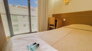 Ein Hotelzimmer mit Bett, Fenster, Stuhl und zwei Flaschen auf dem Bett.