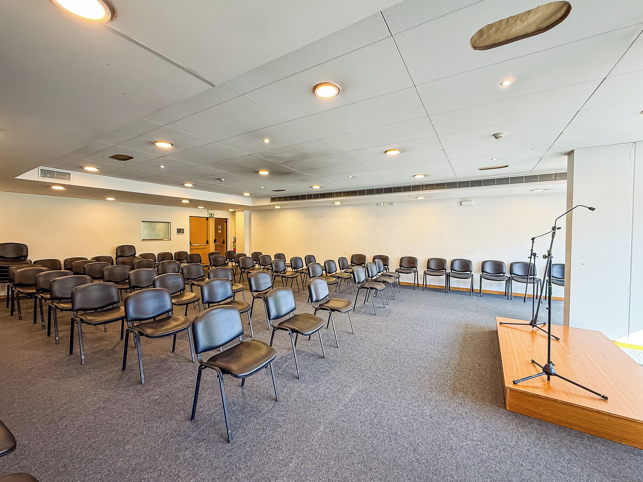 A conference room with rows of chairs, a podium, and ceiling lights.