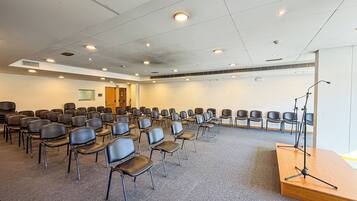 Un salón de conferencias con hileras de sillas, un atril y luces en el techo.
