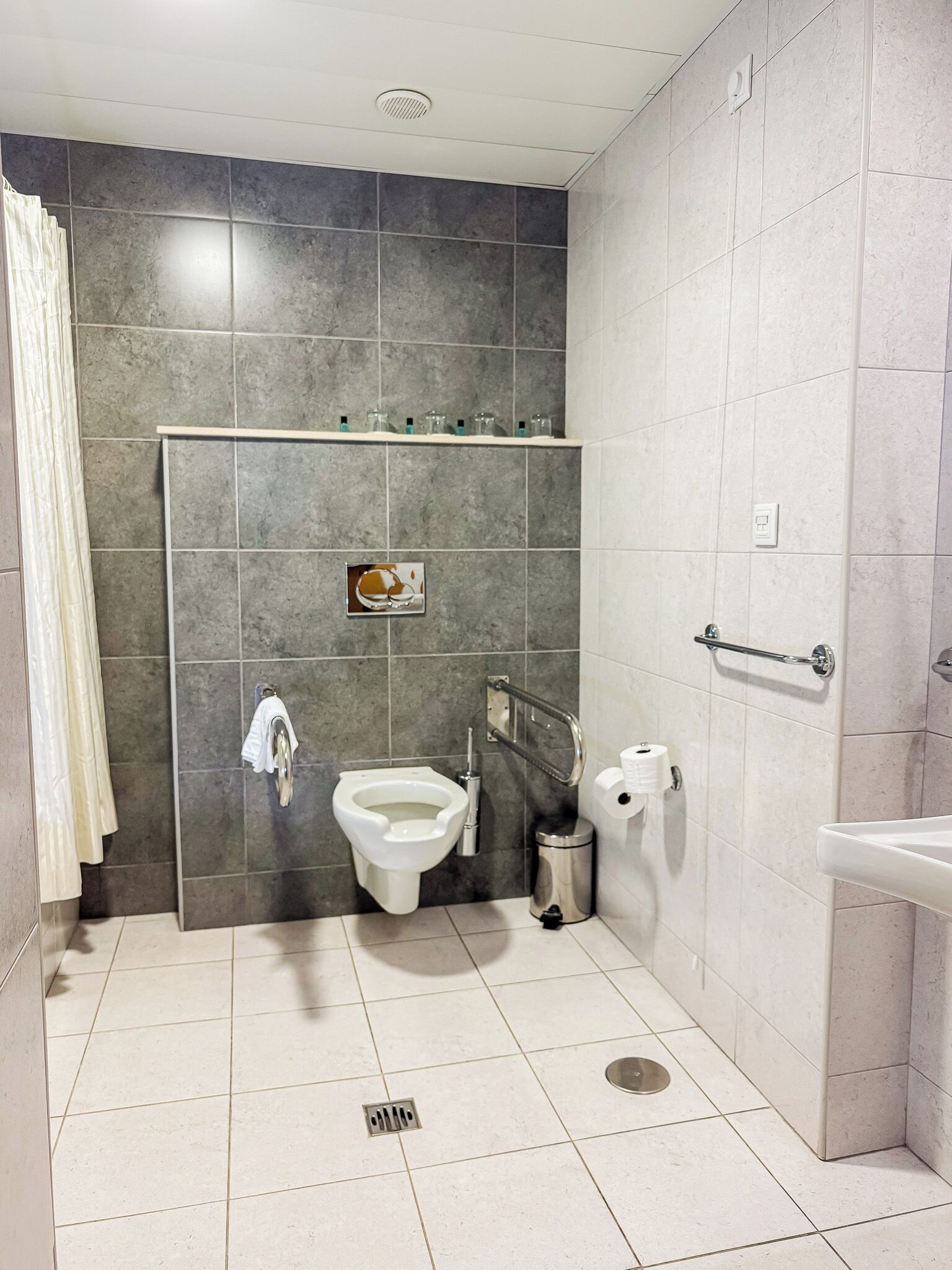 Un baño moderno con inodoro, bidé, secador de manos y repisas con artículos de tocador.