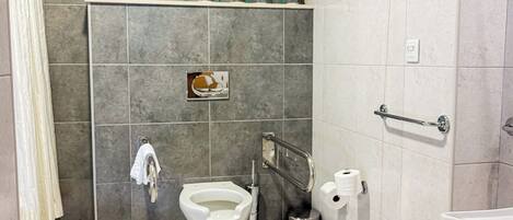 Un baño moderno con inodoro, bidé, secador de manos y repisas con artículos de tocador.