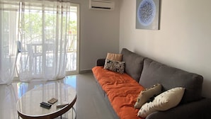 Uma sala de estar moderna com um sofá cinzento, mantas laranja e uma mesa de vidro redonda.