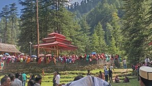 A red-roofed pavilion surrounded by a crowd of people in a forested area.