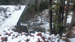 A snow-covered landscape with a building, trees, and a distant view of a valley.