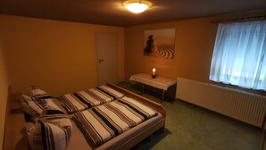 Ein Schlafzimmer mit Bett, Nachttisch, Lampe, Fenster mit Vorhängen, Heizkörper und einer Tür.