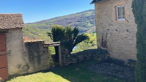 Edifici de pedra amb una finestra i una porta, envoltat d'una zona verda i un mur de pedra.