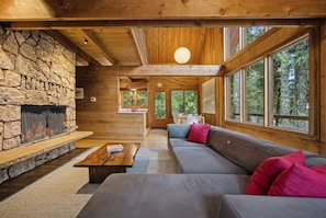 A log cabin interior with a stone fireplace, wooden ceiling beams, and large windows. - Holzhutte - Mid-century alpine retreat - Hot tub (Government Camp)
