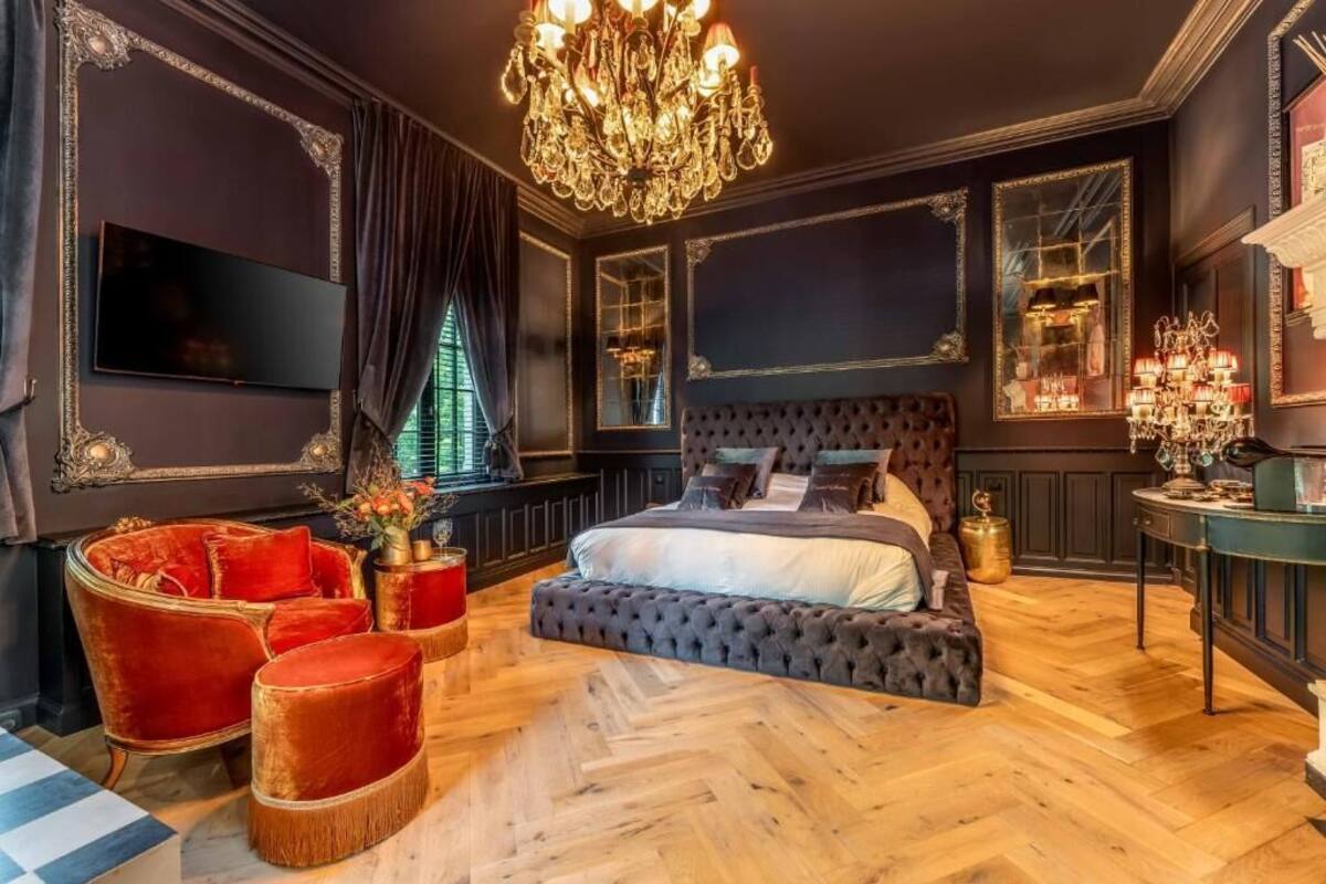 Une chambre à coucher luxueuse, dotée d’un grand lit, d’une télévision, d’un lustre et de décorations murales raffinées.
