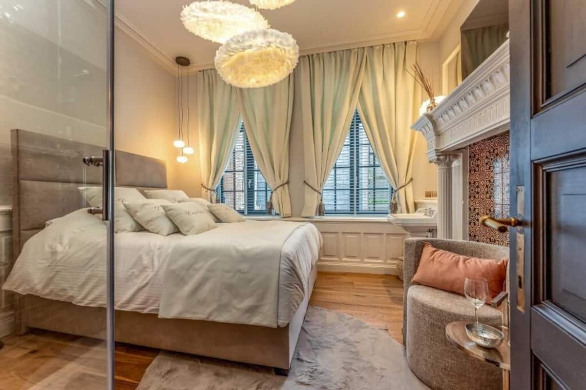 Une chambre à coucher avec un lit, une chaise, une cheminée et une fenêtre avec des rideaux.