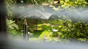 Un patio con mesa y sillas, una sombrilla y vistas al jardín.