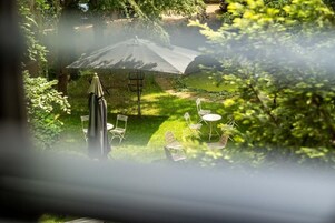 Un patio con mesa y sillas, una sombrilla y vistas al jardín.