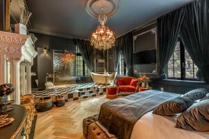 Un dormitorio lujoso con una cama grande, una araña, un sillón rojo y un suelo a cuadros.