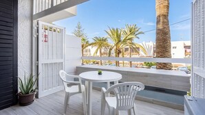 Un balcone con un tavolo e sedie bianche, una pianta in vaso e vista su palme e edifici.