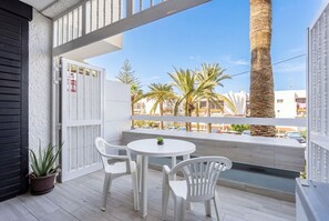 Ein Balkon mit weißem Tisch und Stühlen, einem Blumentopf und Blick auf Palmen sowie Gebäude.