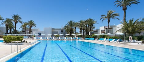 A swimming pool with clear blue water, surrounded by lounge chairs and palm trees.