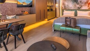 Moderni hotellihuone, jossa on sänky, ruokailutila, keittiö ja seinälle asennettu televisio.