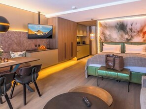 Ein modernes Hotelzimmer mit Bett, Essbereich, Küche und Fernseher an der Wand.