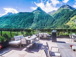 Eine Außenpatio mit Tischen, Stühlen, einem Grill und Blick auf Berge.