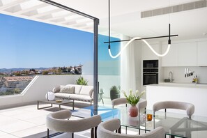 Un apartamento moderno con mesa de vidrio, sofá y sillas, zona de cocina y vistas a la ciudad.