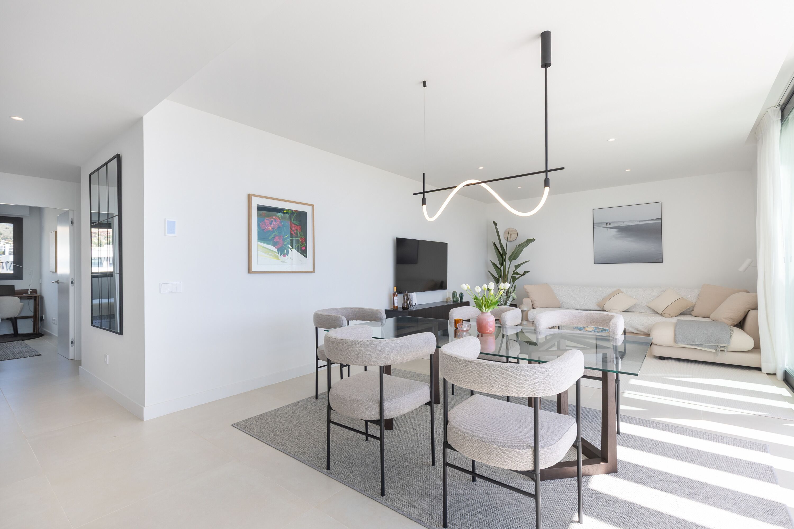 Un salon moderne avec une table à manger en verre, quatre chaises, un téléviseur à écran plat, un canapé et une grande fenêtre.