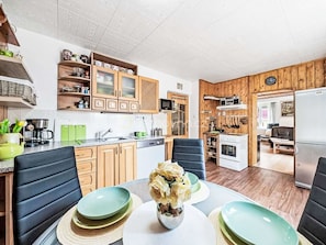 Una cocina moderna con armarios de madera, un comedor con mesa dispuesta para cuatro personas, y una sala de estar con sofá y televisor.
