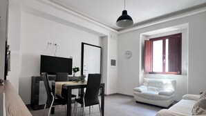 A modern living room with a dining area, a white sofa, a window with curtains, and a ceiling light. - Heart Of Eagle - Dwelling in the historic center with private courtyard (L'Aquila)