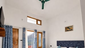 A spacious bedroom with a large bed, a ceiling fan, a wooden door, and a window with curtains.