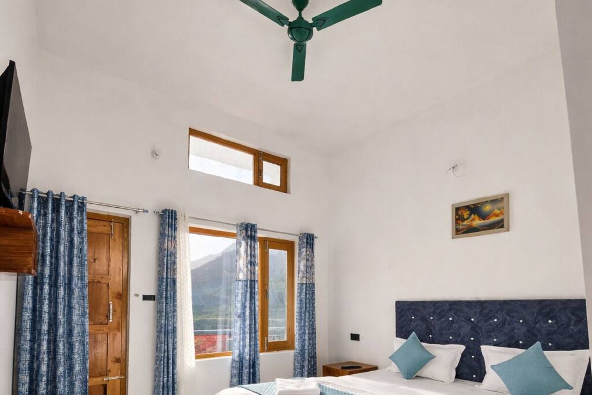 Un dormitorio amplio con una cama grande, un ventilador de techo, una puerta de madera y una ventana con cortinas.