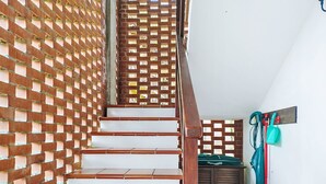 Un escalier avec des marches en bois et une rampe en métal, menant à une pièce dont le sol est recouvert de carreaux et qui est équipée d’une armoire fixée au mur.