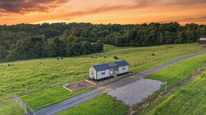 Un paisaje rural con una casa de campo, un camino de grava y un pastizal cercado con ganado pastando.