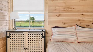 A wooden cabin interior with a bed, a window with a view of a green field, and a radiator. - Cozy stay at Baling Out Farms (Southside)