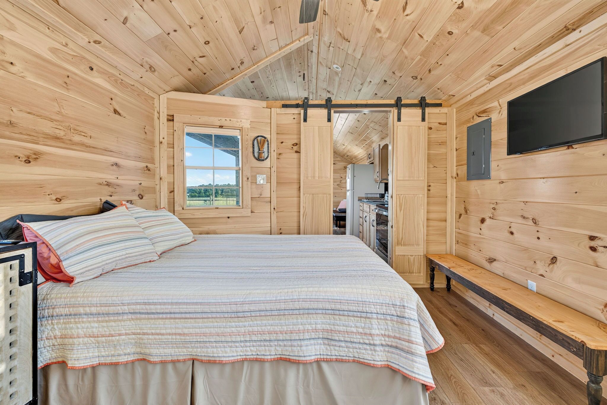 A wooden cabin interior with a bed, a window, and a television.