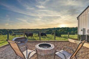 A patio with a fire pit, chairs, and a view of cows in a fenced pasture. - Cozy stay at Baling Out Farms (Southside)