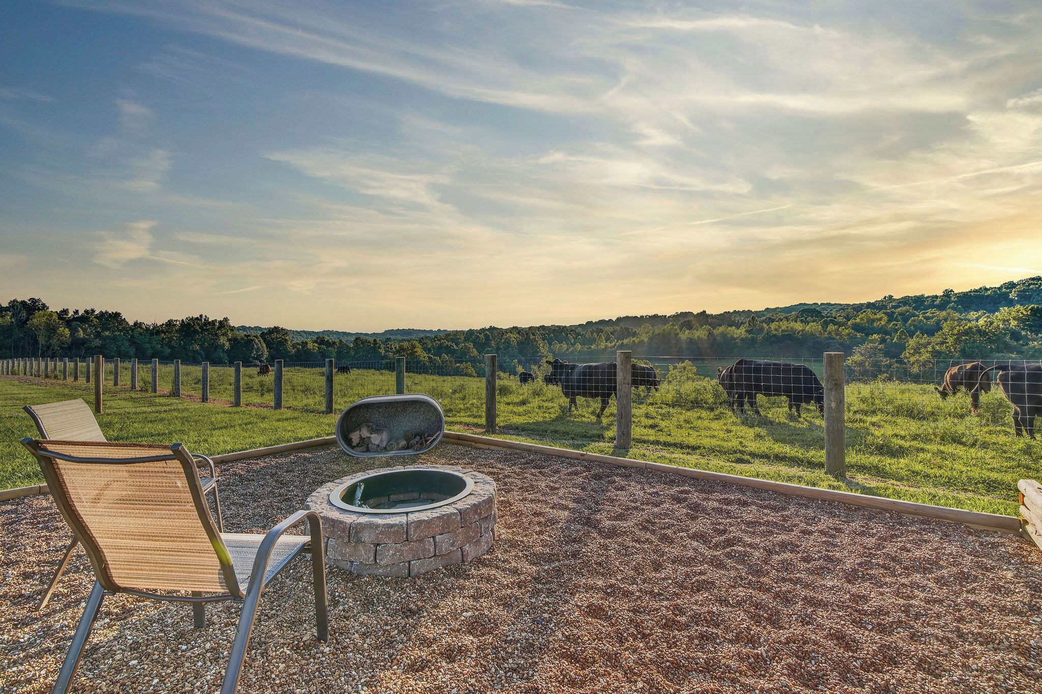 A patio with a fire pit, seating, and a view of cows in a fenced pasture.